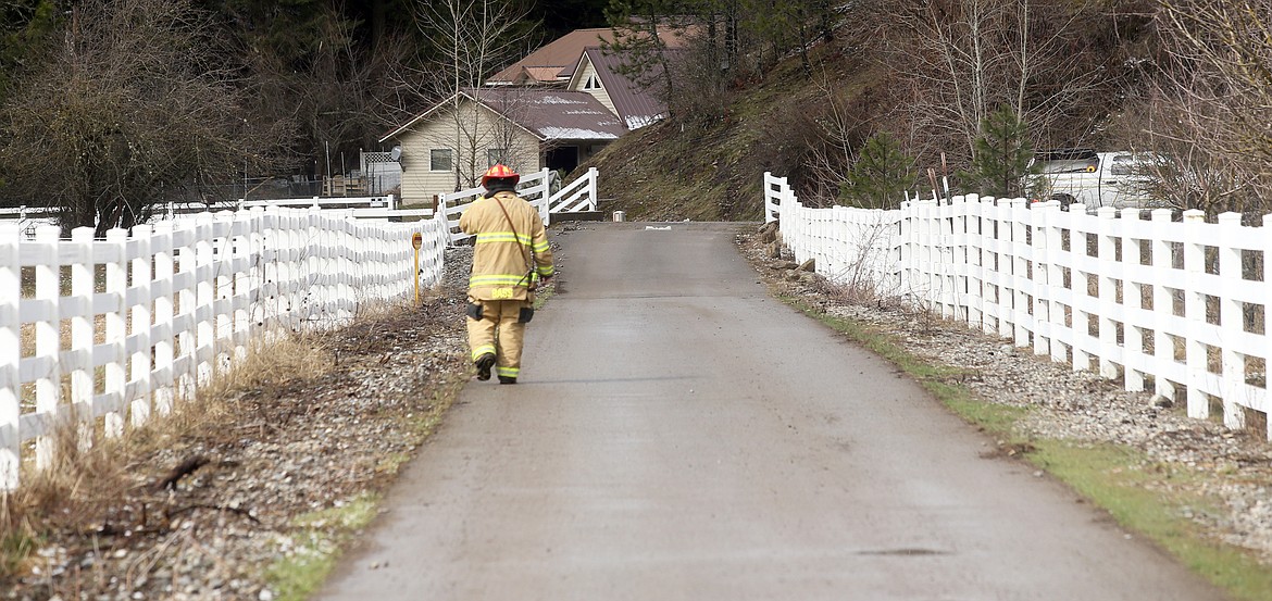 Kootenai County Fire & Rescue firefighter Michael Bass walks down the long drive leading to the home that caught fire on East Fernan Lake Road Thursday.