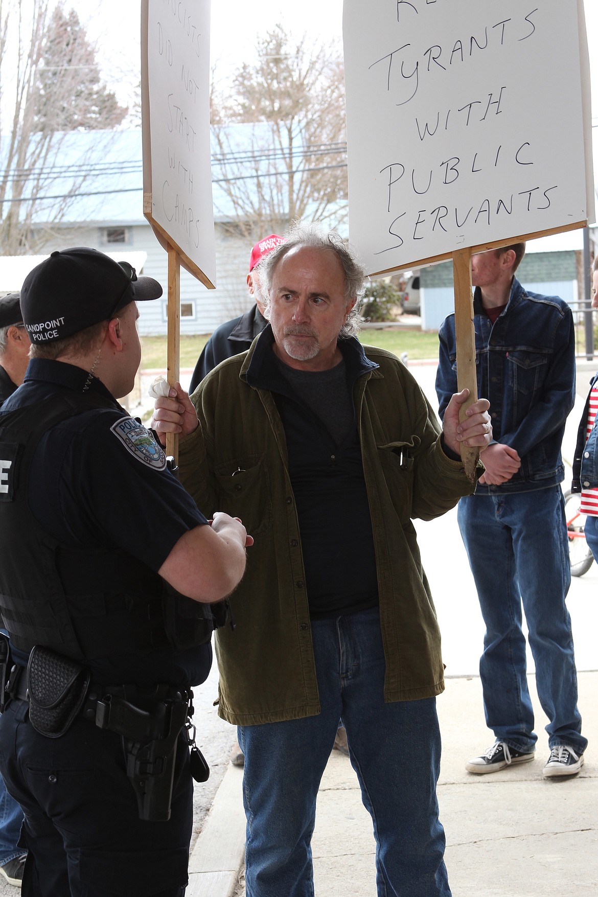 Mask protestor Mark Watson speak with a Sandpoint Police officer at the Sandpoint Library on Saturday. (Photo by KEITH KINNAIRD)