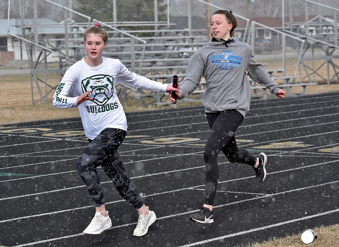 Bulldog runner Bailey Smith accepts the baton handoff from senior captain Mikenna Ells during practice on Monday. (Whitney England/Whitefish Pilot)