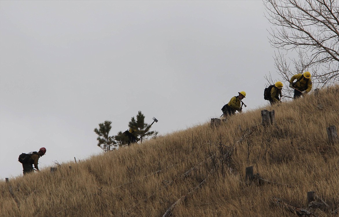 Firefighters battling wildfires in the Black Hills of South Dakota create a trench with axes on a hillside west of Rapid City on Monday, March 29, 2021. The blaze that started on property near the town of Nemo had burned at least 11/2 square miles and led to the evacuation of 400 homes as of Monday afternoon. Officials say two homes and numerous outbuildings were destroyed on a day when wind gusts reached 72 mph. (Siandhara Bonnet/Rapid City Journal via AP)