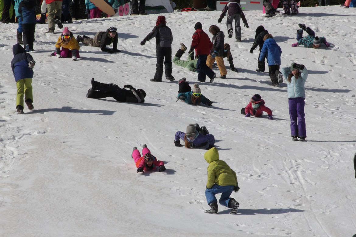 Children slide and roll down the hill while waiting for their turn on the toboggans.