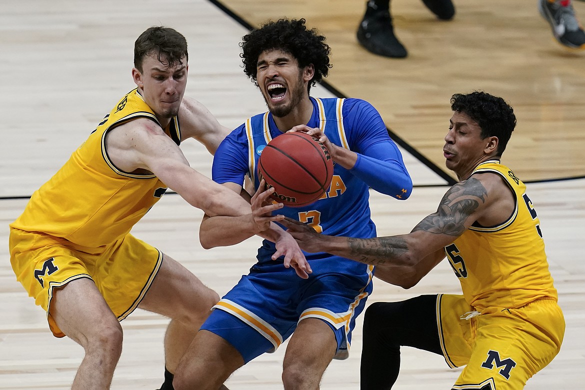 UCLA guard Johnny Juzang is fouled while catching a pass between Michigan guard Franz Wagner, left, and guard Eli Brooks, right, during the second half of an Elite 8 game in the NCAA men’s college basketball tournament at Lucas Oil Stadium, Tuesday, March 30, 2021, in Indianapolis. (AP Photo/Michael Conroy)