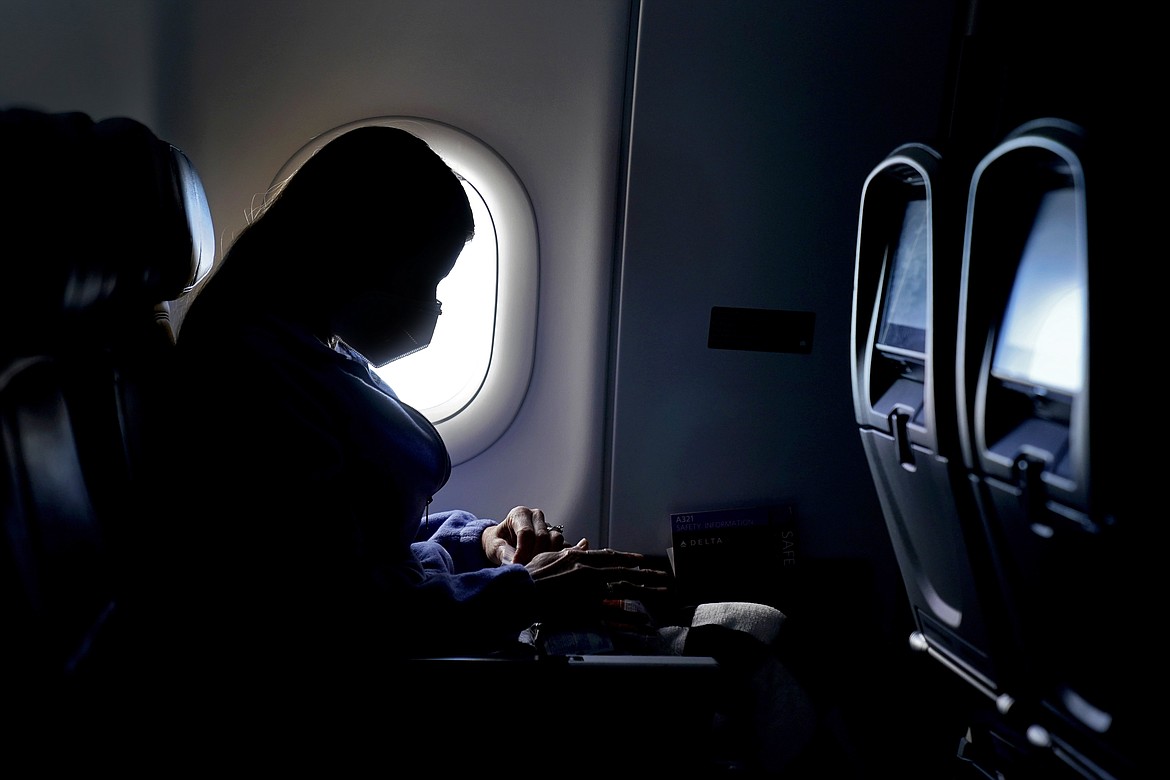 In this Wednesday, Feb. 3, 2021 file photo, a passenger wears a face mask during an airline flight after taking off from Atlanta. On Friday, April 2, 20201, the Centers for Disease Control and Prevention updated its guidance to say fully vaccinated people can travel within the U.S. without getting tested for the coronavirus or going into quarantine afterward.