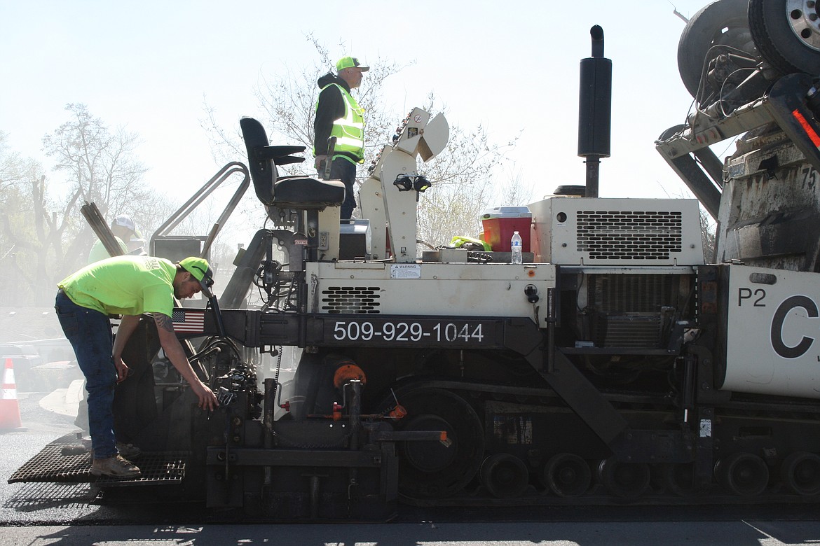 Hunter Bair (left) monitors the distribution of asphalt while paving a section of Valley Road Northwest Monday. Curtis Hawk is the driver.