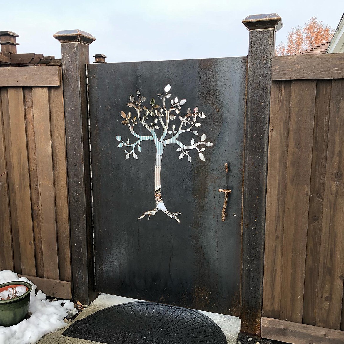An example of a metal gate door crafted by Chris Ball in Moses Lake, complete with aluminum handle, lock  and door stopper cut to resemble the bark of a tree.