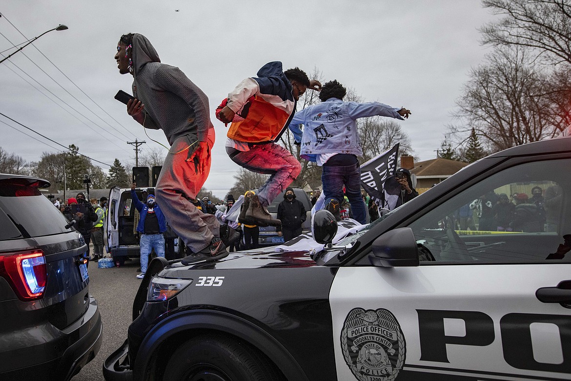 Men jump on the hood of a police car after a family said a man was shot and killed by law enforcement on Sunday, April 11, 2021, in Brooklyn Center, Minn.