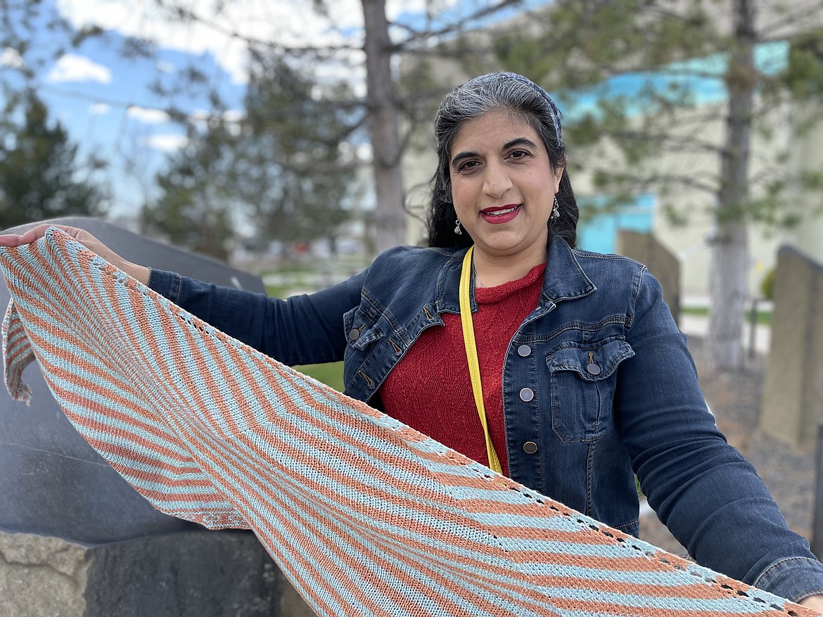 Ranée Mueller, knitter, pattern designer and blogger, holds up a shawl she knitted and designed while wearing a red sweater and a blue headscarf she knitted.