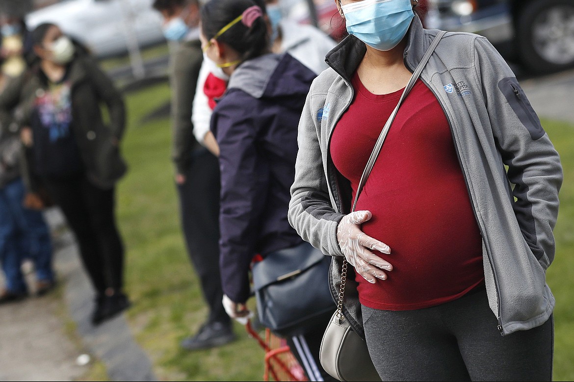 In this Thursday, May 7, 2020 file photo, a pregnant woman wearing a face mask and gloves holds her belly as she waits in line for groceries with hundreds during a food pantry sponsored by Healthy Waltham for those in need due to the COVID-19 virus outbreak, at St. Mary's Church in Waltham, Mass. One of the largest reports on Moderna or Pfizer COVID-19 vaccination in pregnancy bolsters evidence that it is safe although more rigorous research is needed. The new evidence from researchers at the Centers for Disease Control and Prevention was published Wednesday, April 21, 2021, in the New England Journal of Medicine. Johnson & Johnson’s now paused vaccine was not included.