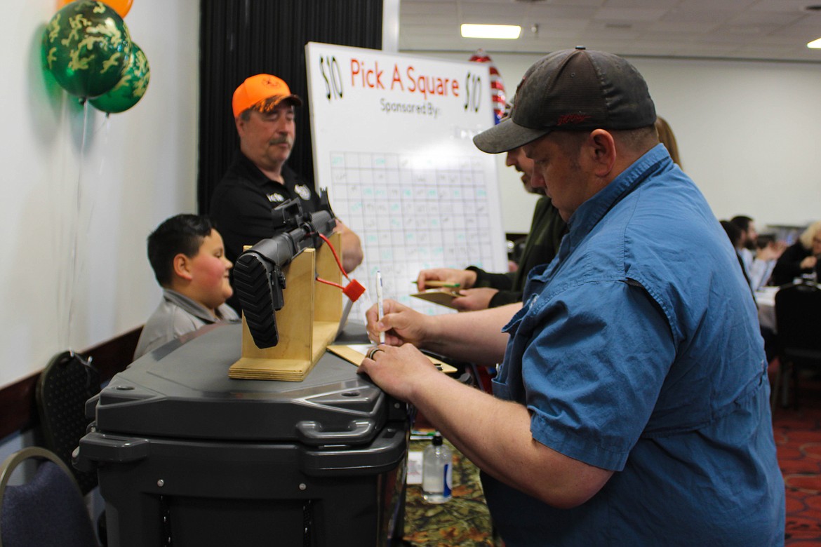 Youth Outdoors Unlimited secretary Martin Monsey (orange hat) displays an AR-10 as people place bids for the silent auction on Saturday.