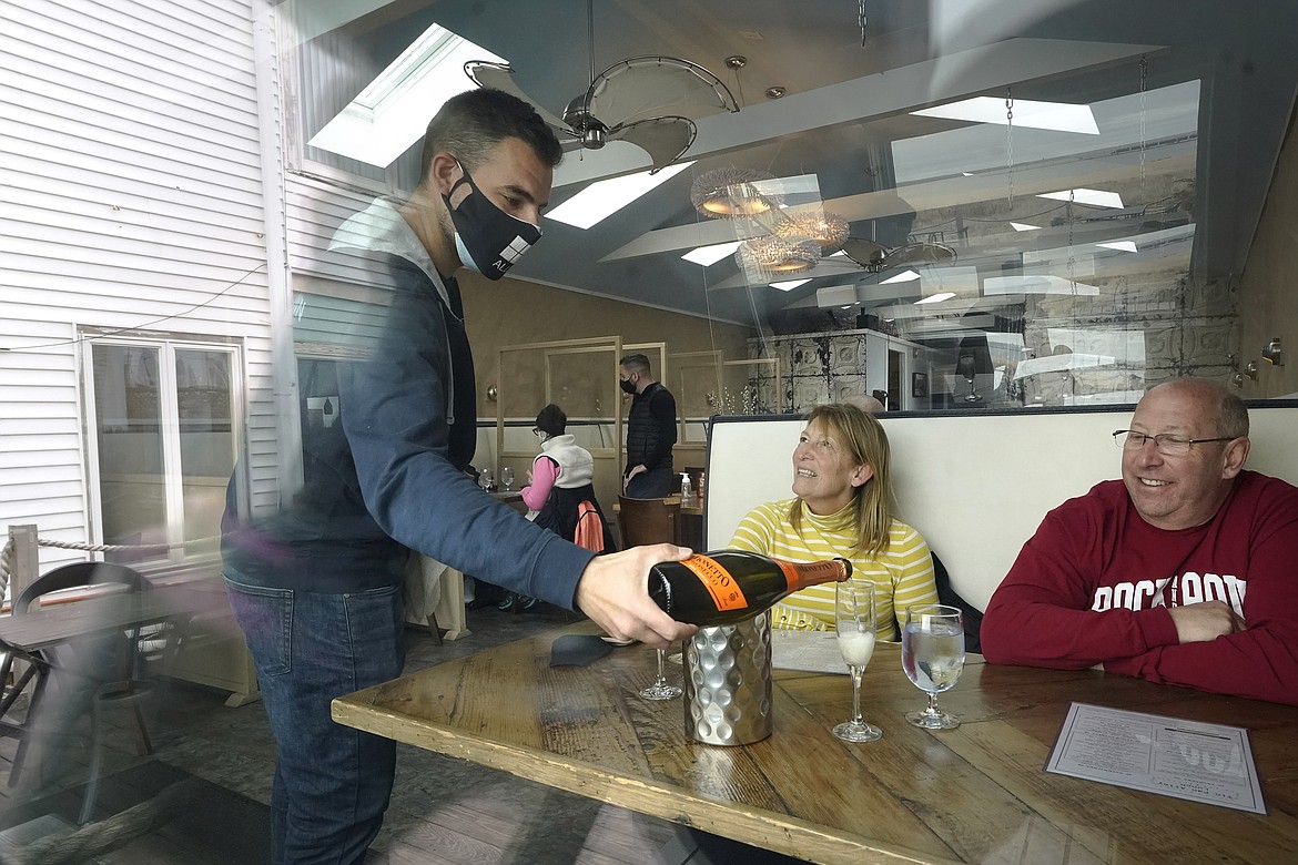 Bartender Denis Angelov, of Provincetown, Mass., left, serves sparking wine to Julie Skaller, left, and her husband David Skaller, right, both of Brewster, N.Y., at Tin Pan Alley restaurant, Tuesday, April 6, 2021, in Provincetown. Hotels, restaurants and other businesses in tourist destinations are warning that hiring challenges during the coronavirus pandemic could force them to pare back operating hours or curtail services just as they’re eyeing a bounce-back summer.