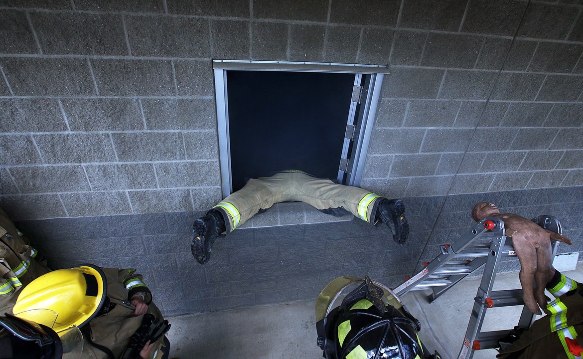 KCFR firefighter Shea Vucinich uses his legs to support himself as he demonstrates how to enter a smoky building on Tuesday at the KCFR Fire Training Center on Seltice Way f