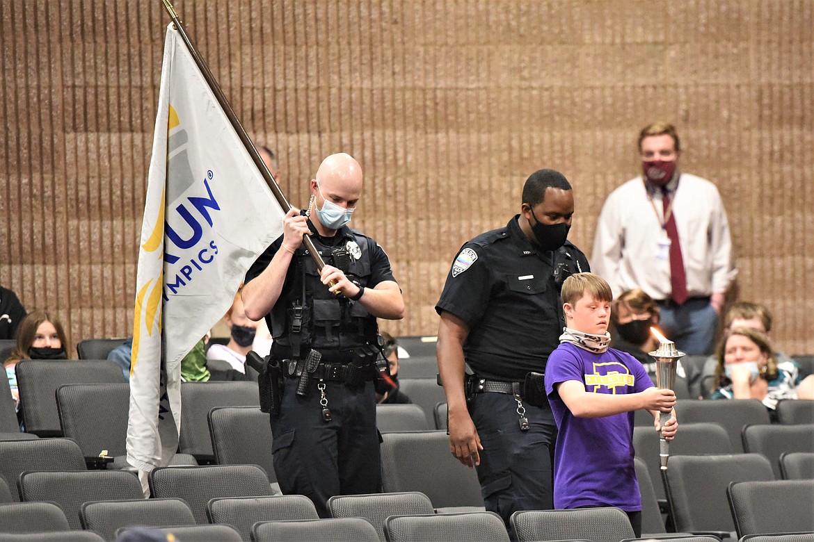 Kyler Gage carries a lit torch through the Polson High School auditorium in front of Polson Police Officer Kyle Cooper, left, and Det. Hazeez Rafiu. (Scot Heisel/Lake County Leader)