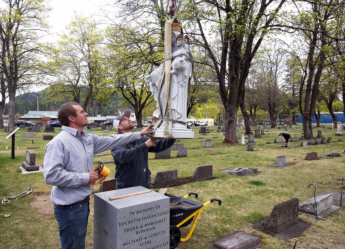 Brandon Mitchell, left, and TJ Harris with Memorial Monuments lower the new statue of Mary and Baby Jesus into place at St. Thomas Cemetery on Friday.