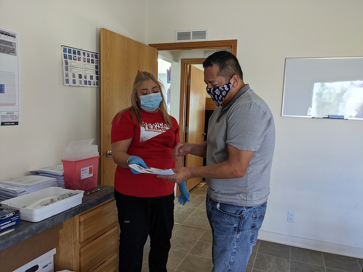 State Representative Alex Ybarra hands over his paperwork to Sara Maldonado of Medical Teams International before receiving his first COVID-19 vaccination shot in Royal City Wednesday