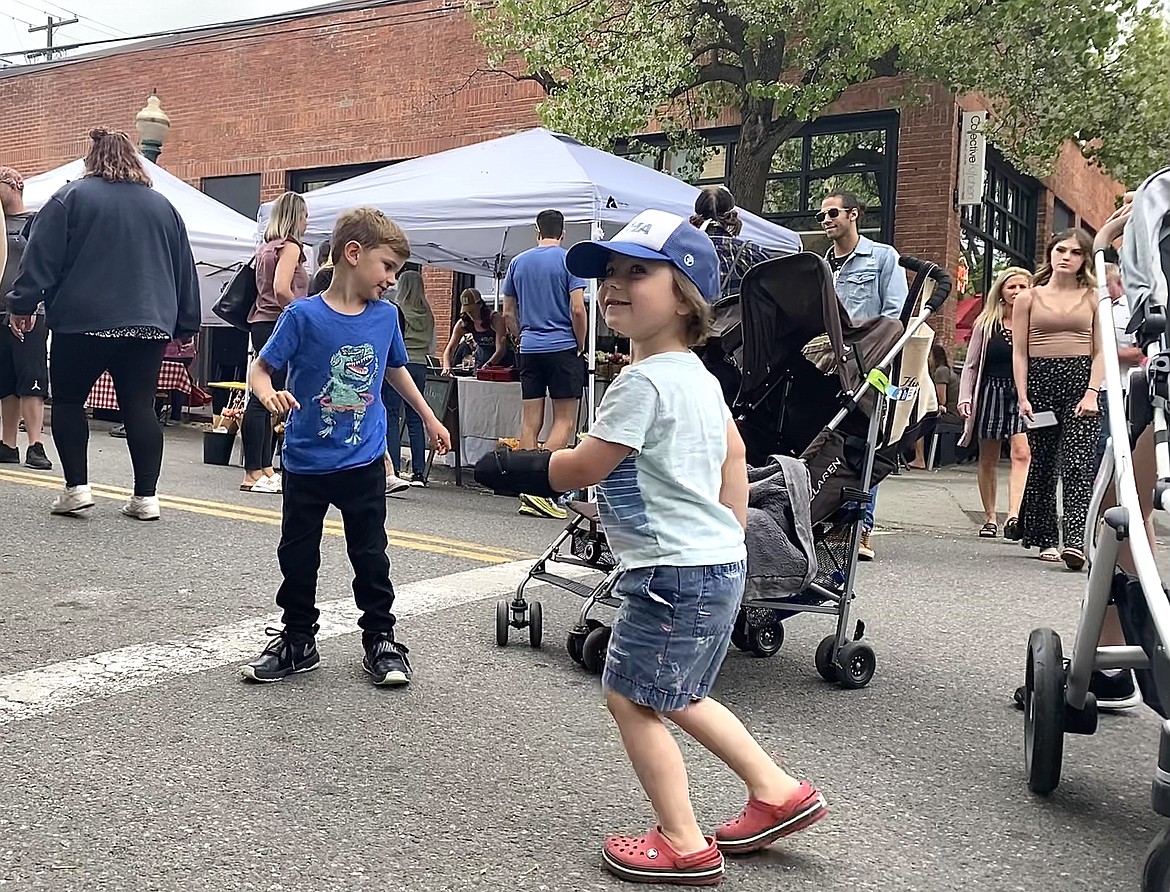 Finn Livingston, right, and his friend Harry show off their dance moves at the Wednesday farmers' market as community members walk by. (MADISON HARDY/Press)