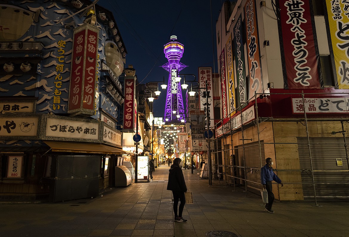 In this April 19, 2021, file photo, a restaurant staff member, center, stands in the middle of a street to promote her establishment at one of the famous commercial districts in Osaka, western Japan, as some of the businesses have closed under the government measures against the coronavirus. Hospitals in Osaka, Japan’s third-biggest city and only 2 1/2 hours by bullet train from Summer Olympics host Tokyo, are overflowing with coronavirus patients. About 35,000 people nationwide - twice the number of those in hospitals - must stay at home with the disease, often becoming seriously ill and sometimes dying before they can get medical care.