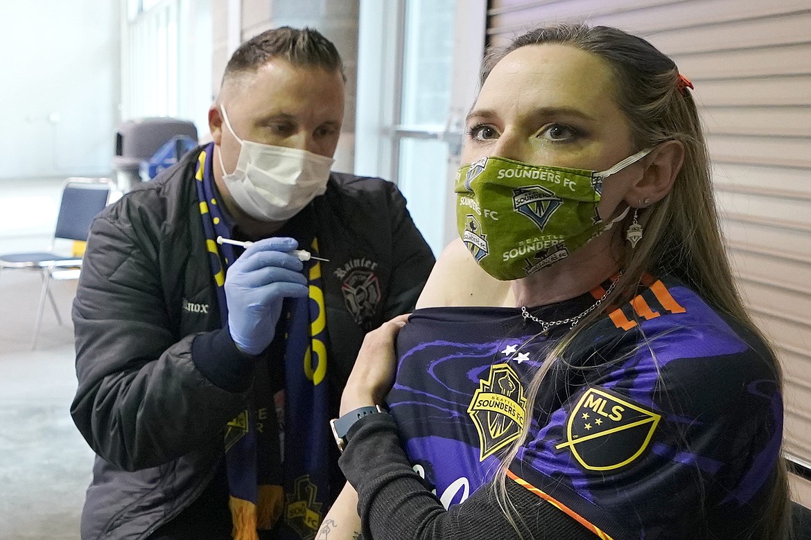 In this May 2, 2021, file photo, Stephanie Birman, right, a Seattle Sounders season ticket holder, wears a Sounders mask, jersey and earrings as she gets the Johnson & Johnson COVID-19 vaccine at a clinic in a concourse at Lumen Field prior to an MLS soccer match between the Sounders and the Los Angeles Galaxy. On Thursday, May 20, 2021, authorities in King County, Wash., which includes Seattle, said all people should continue wearing masks indoors until 70% of people in the county 16 and older are fully vaccinated.