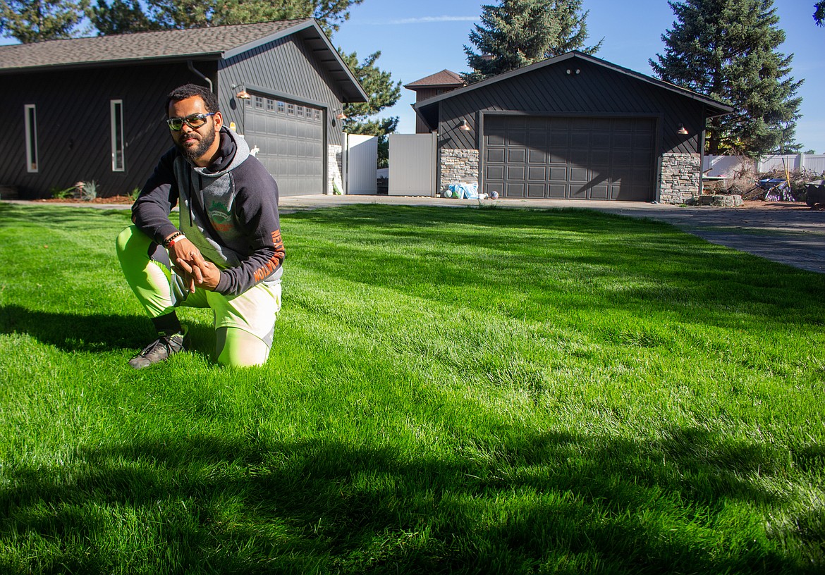 Domanique Benham, owner of EnvyUs Lawn Care, kneels in a freshly trimmed front lawn in Moses Lake.