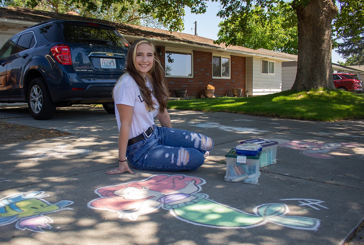 Moses Lake High School senior Tessa Pyle sits in her driveway in Moses Lake on Tuesday afternoon beside one of the many chalk artworks she's created since picking up the hobby shortly after the pandemic came into affect last spring.