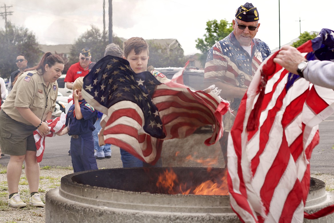 Cub Scout Ukiah Balback, 10, throws an unserviceable flag into the flames under the direction of Sergeant-at-Arms Tim Shaw, right, at the flag day ceremony Saturday morning at the American Legion post in Post Falls