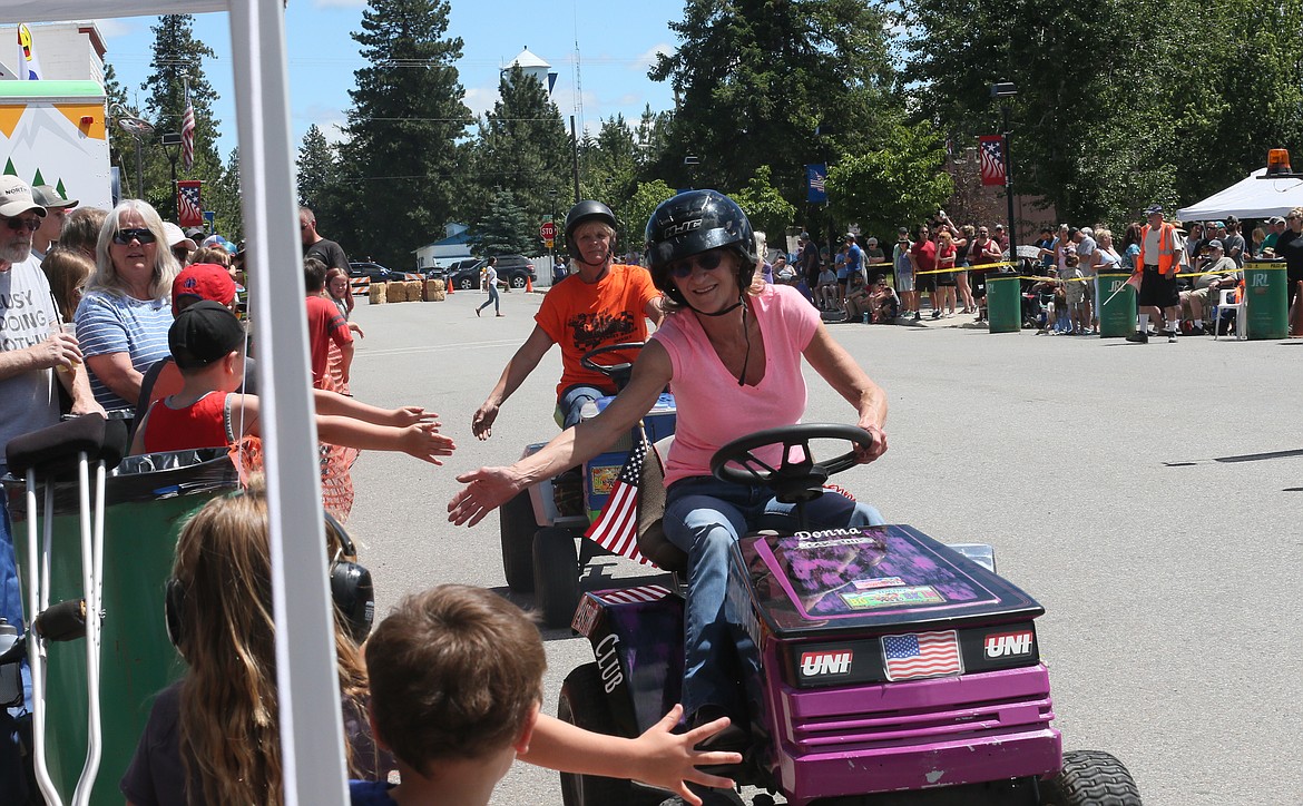 Donna Davis, front, and Jeanne Ewing high-five kids along Maine Street in Spirit Lake as they return to the driver's pit during the Big Back-In lawnmower races on Sunday.