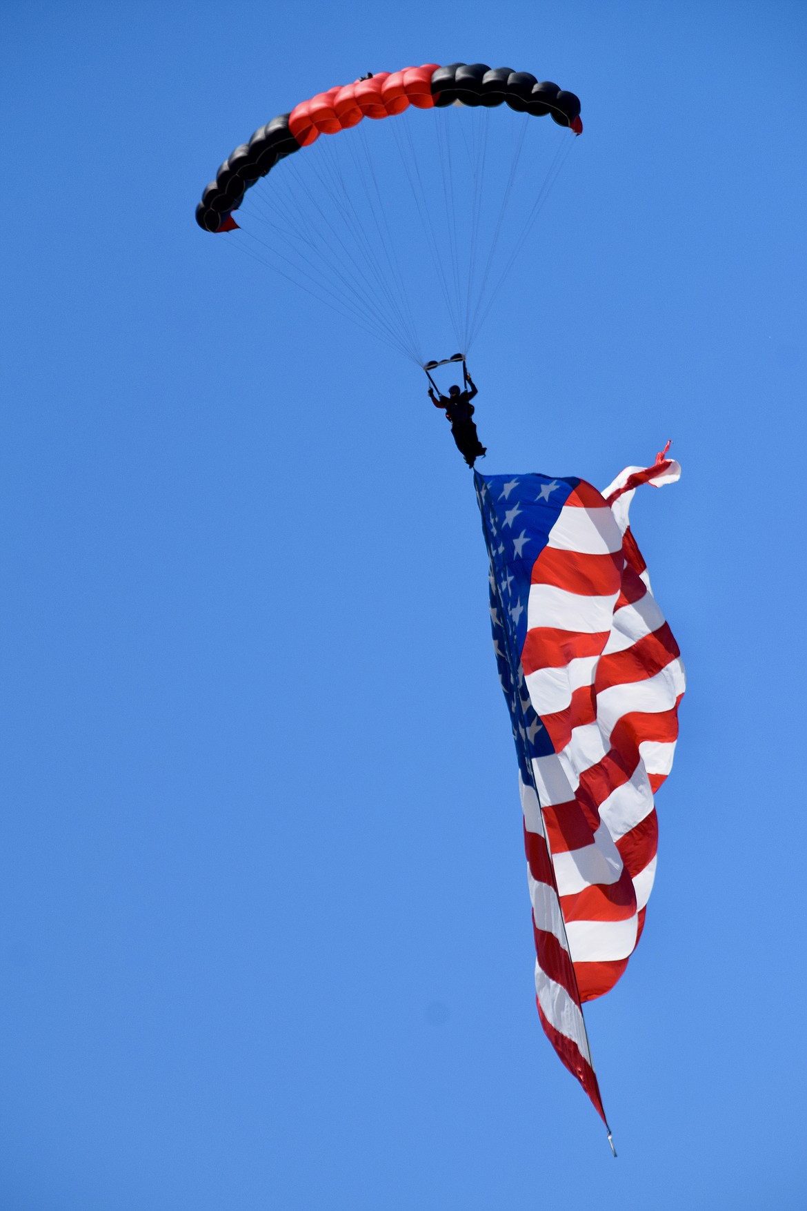 A member of the U.S. Army Special Forces Command’s Black Daggers parachute team trails a giant American flag on a descent during the 2021 Moses Lake Airshow on Friday.