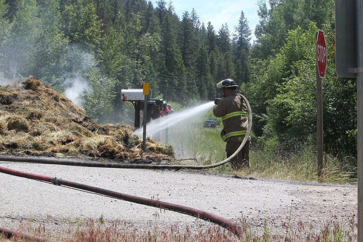Libby volunteer fire fighters hose down a pile of burning hay that caught fire on state Highway 37 north of Libby. Fire Chief Steve Lauer said a mechanical malfunction in at least one of the wheels of the trailer carrying the hay sparked the flames. (Will Langhorne/The Western News)