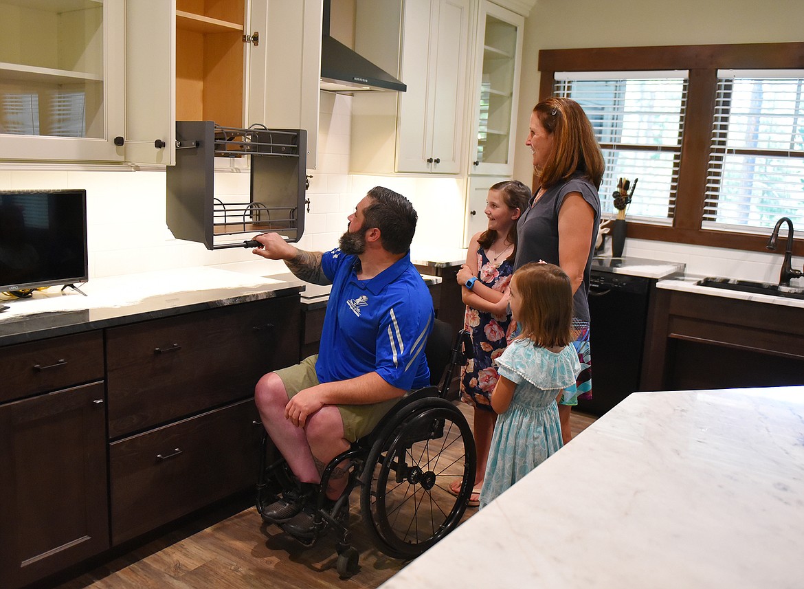 Austin Reese, while his wife Charity and daughters Nadia and Aspen watch, checks out the specially adapted cupboard in his new home on Thursday morning. The home includes several adaptive features, particularly in the kitchen and bathroom, along with voice-activated and touchless smart controls. (Heidi Desch/Whitefish Pilot)