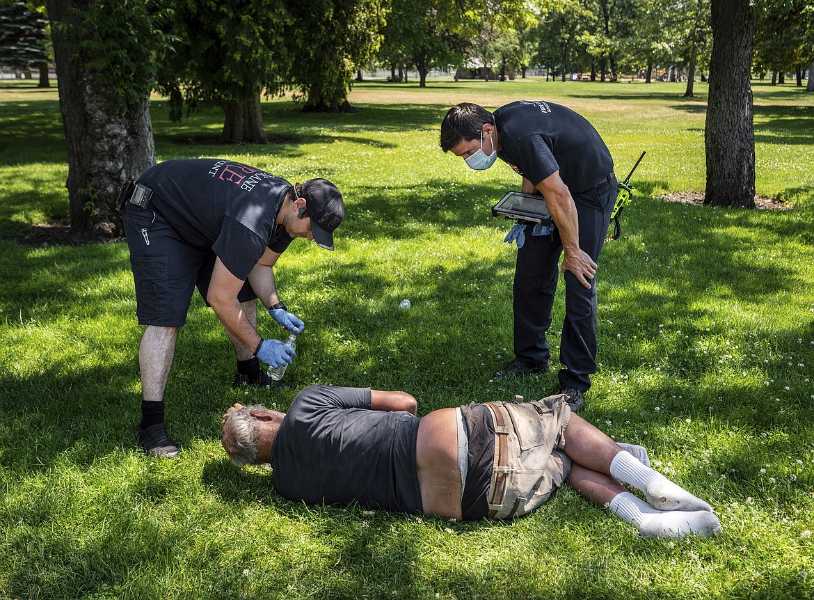 With the temperature well over 100 degrees, Spokane firefighter Sean Condon, left, and Lt. Gabe Mills, assigned to the Alternative Response Unit from Station 1, check on the welfare of a man in Mission Park in Spokane, Wash., on Tuesday, June 29, 2021. The special fire department unit, which responds to low-priority calls, has been busy during this week's heat wave. (Colin Mulvany/Spokesman-Review via AP)