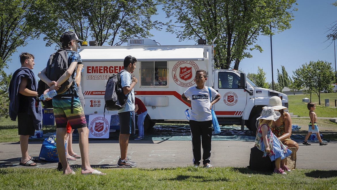 A Salvation Army emergency medical services vehicle is set up as a cooling station as people line up to get into a splash park while trying to beat the heat in Calgary, Alberta, on Wednesday, June 30, 2021. Environment Canada warns the torrid heat wave that has settled over much of western Canada won't lift for days. (Jeff McIntosh/Canadian Press via AP)