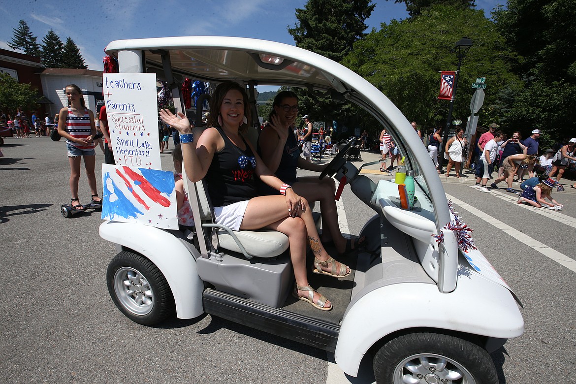 Colleen Attebury, left, and Devra Witzel with the Spirit Lake Elementary PTO sit in a covered cart during the parade on Sunday.