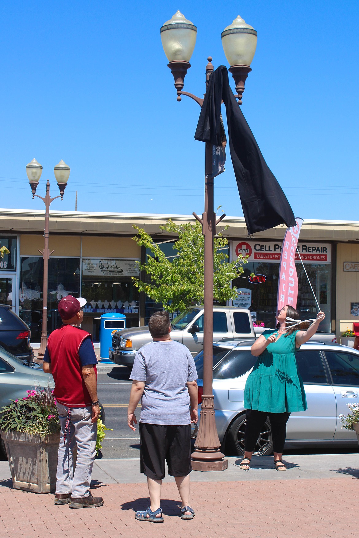 Denise Kinder removes a cover to reveal a commemorative banner in downtown Moses Lake on Tuesday.