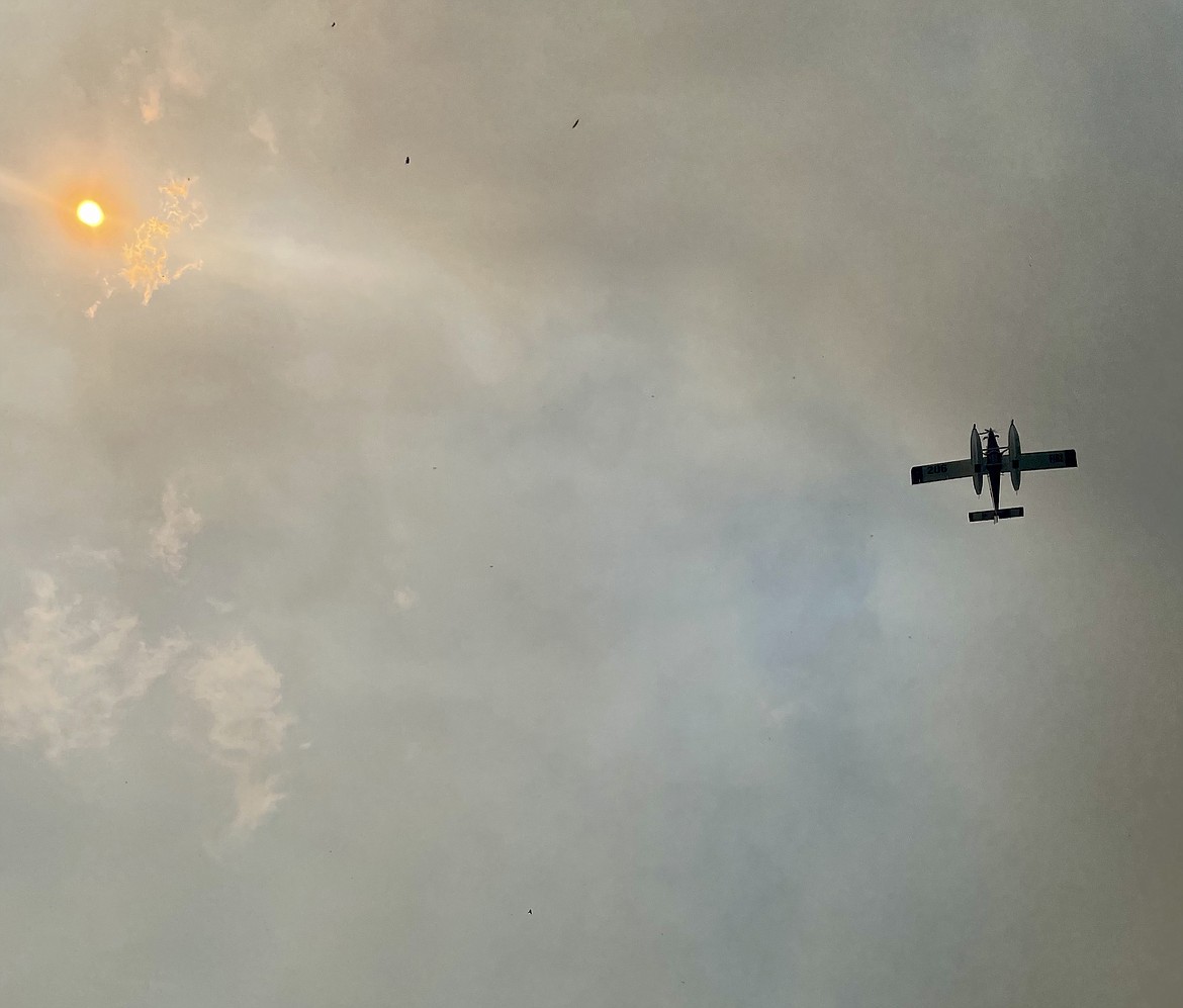 Smoke blots out the sun while ash rains from the sky as an airplane makes an overhead pass of the Mission Flats Fire.