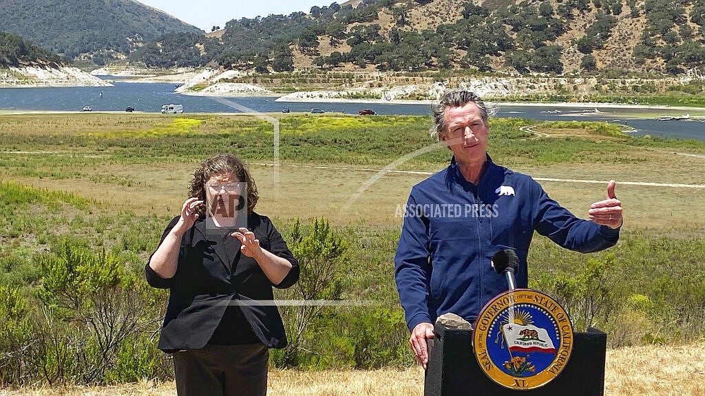 Gov. Gavin Newsom and interpreter Julia Townsend stand at the edge of a diminished Lopez Lake near Arroyo Grande, Calif., Thursday, July 8, 2021. Newsom has asked people and businesses in the nation's most populous state to voluntarily cut how much water they use by 15% amid a drought. Newsom's request is not an order. But it demonstrates the growing challenges of a drought that will only worsen throughout the summer and fall and is tied to recent heat waves. (David Middlecamp/The Tribune (of San Luis Obispo) via AP)