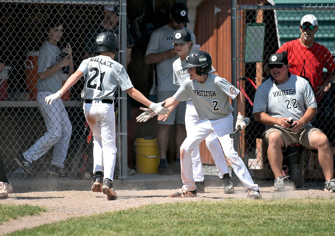 Whitefish player Cullen Wallace celebrates scoring a run with high fives to Drew Queen (front) and Luke Dalen (back) in a baseball game Friday against Mission during the Cal Ripken 12U Montana State Tournament in Whitefish. (Whitney England/Whitefish Pilot)