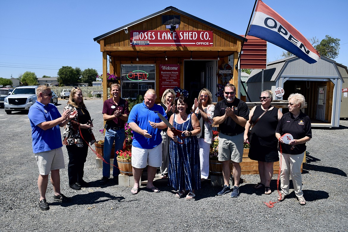 Moses Lake Shed Company owner Cherity Mengelos (holding the giant scissors) and her husband Jon, flanked by members of the Moses Lake Chamber of Commerce, officially cut the ribbon Thursday in a short ceremony in front of their business at 1800 W. Broadway Ave.