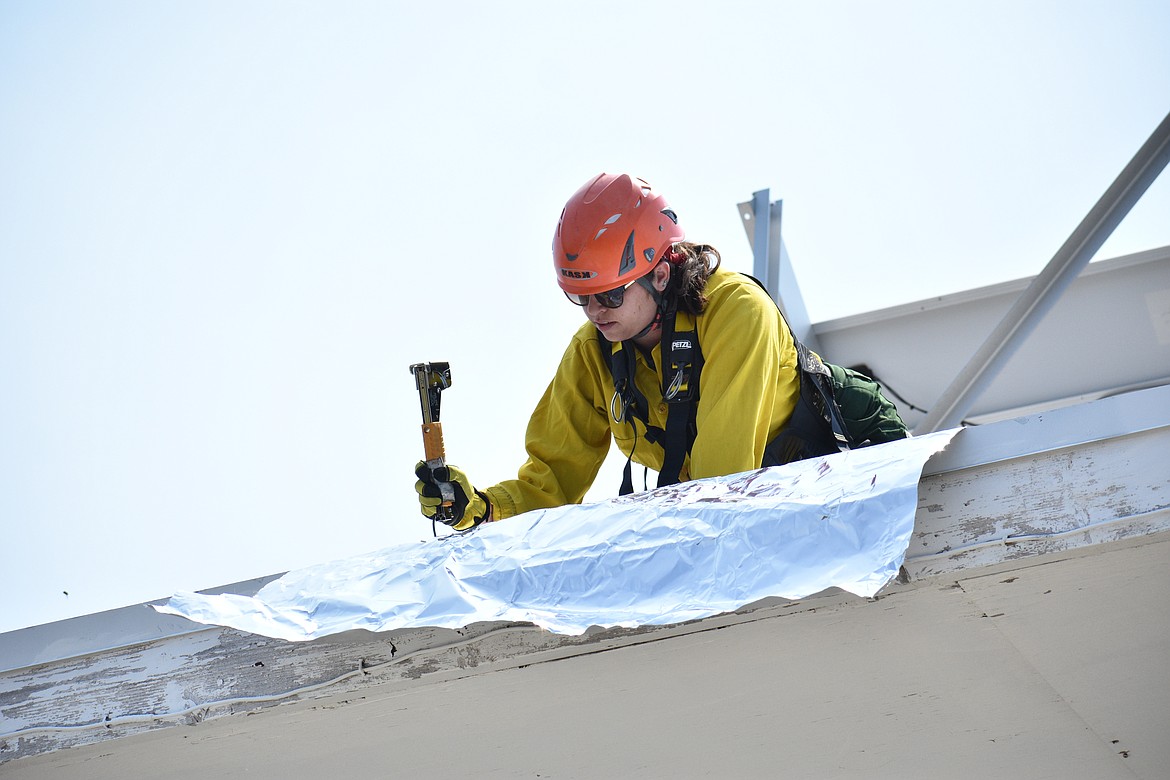 Jessica Goodwin staples a piece of wrap to the lookout tower roof on Saturday.