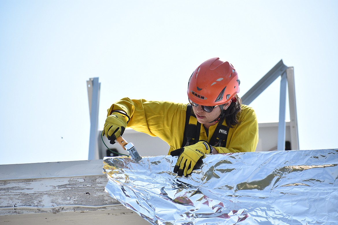 Jessica Goodwin staples a piece of wrap to the lookout tower roof.