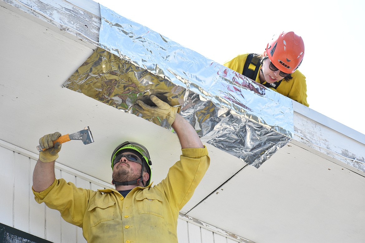 Christian Goodlander, left, staples a piece of wrap to the Lunch Peak Lookout while Jessica Goodwin secures it to the roof of the tower on Saturday.