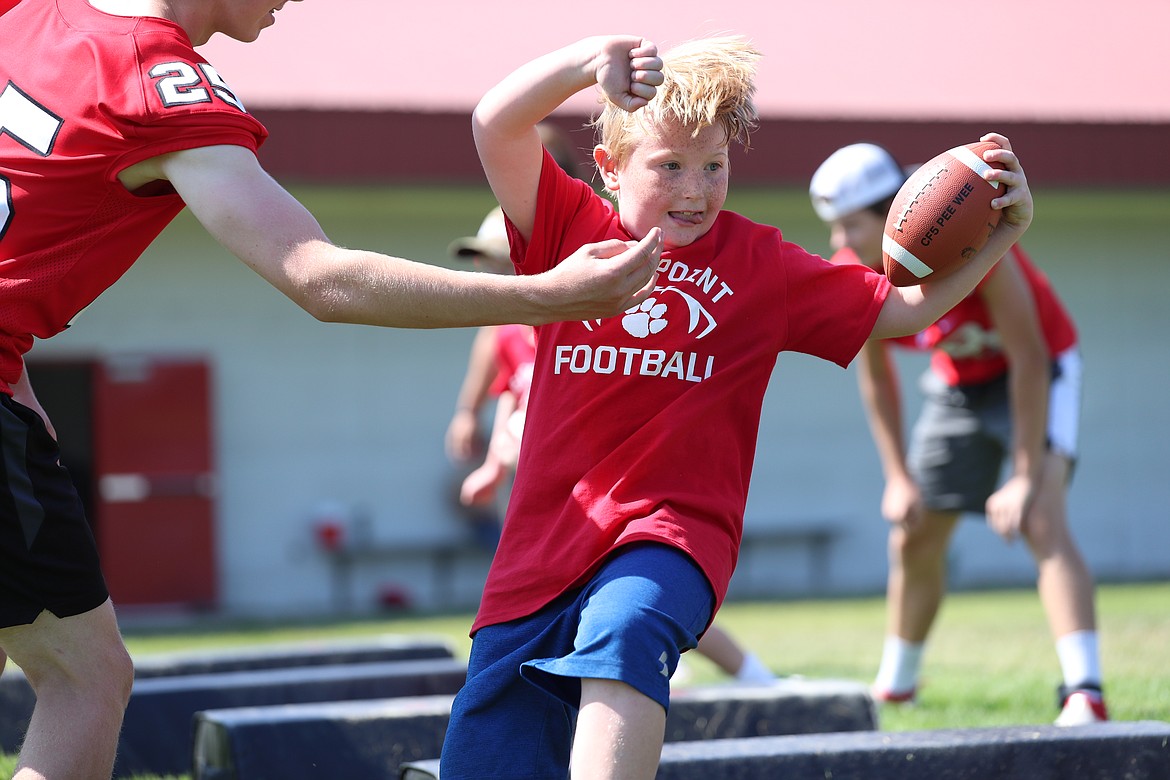 A camper jukes past the outstretched arm of a varsity player during running backs drills on Friday.