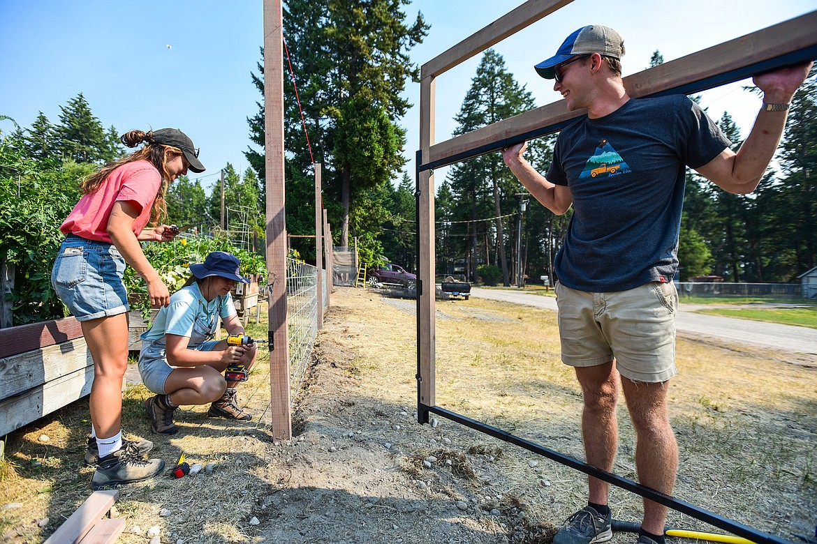 Architecture students, Julia Plapper, left, from Munich, Germany and Alexis Warner, center, from Auburn University, install a hinge for a gate held by William Scurry, right, from The University of North Carolina at Charlotte, for the exterior fencing of the Lakeside Community Garden outside the Living Church at Lakeside on Friday, July 30. The three are part of 100 Fold Studios' summer internship program for architecture students interested in nonprofit careers. (Casey Kreider/Daily Inter Lake)