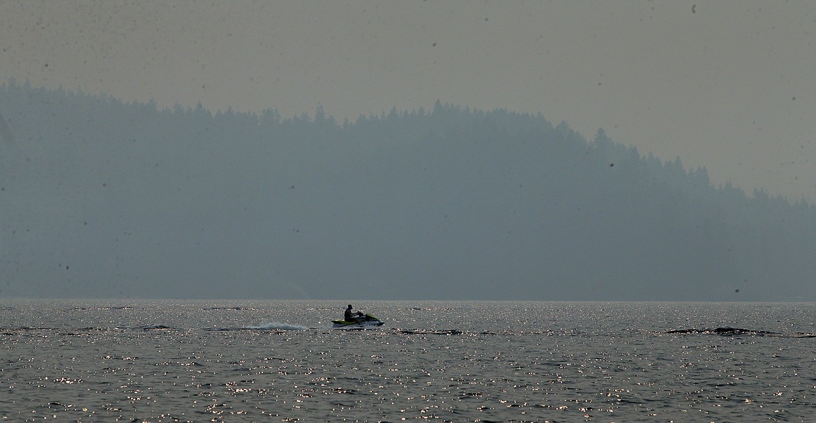 A man rides a personal watercraft on Lake Coeur d'Alene Monday, while smoke covers the mountains in the background.