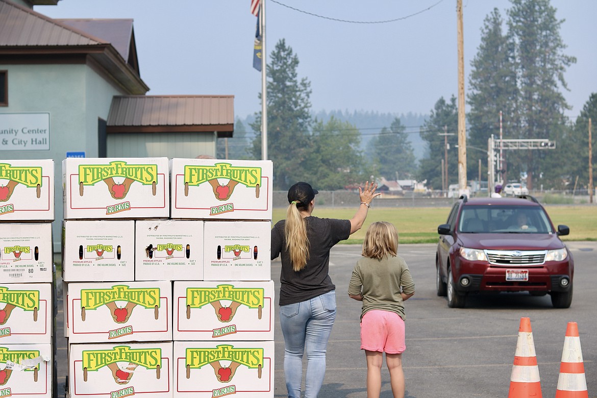 Lynn Pampaian from Athol and her daughter, Helena Nimmo, 8, wave to a car approaching the apple distribution drive through at the ABC Food Bank. HANNAH NEFF/Press