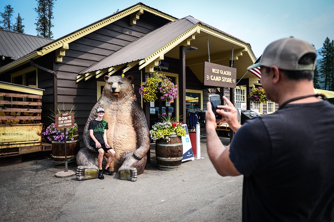 Hayri Barutcu, from Denver, takes a picture of his son Ryan on a bear in front of the West Glacier Camp Store on Wednesday, Aug. 4, 2021. (Casey Kreider/Daily Inter Lake)