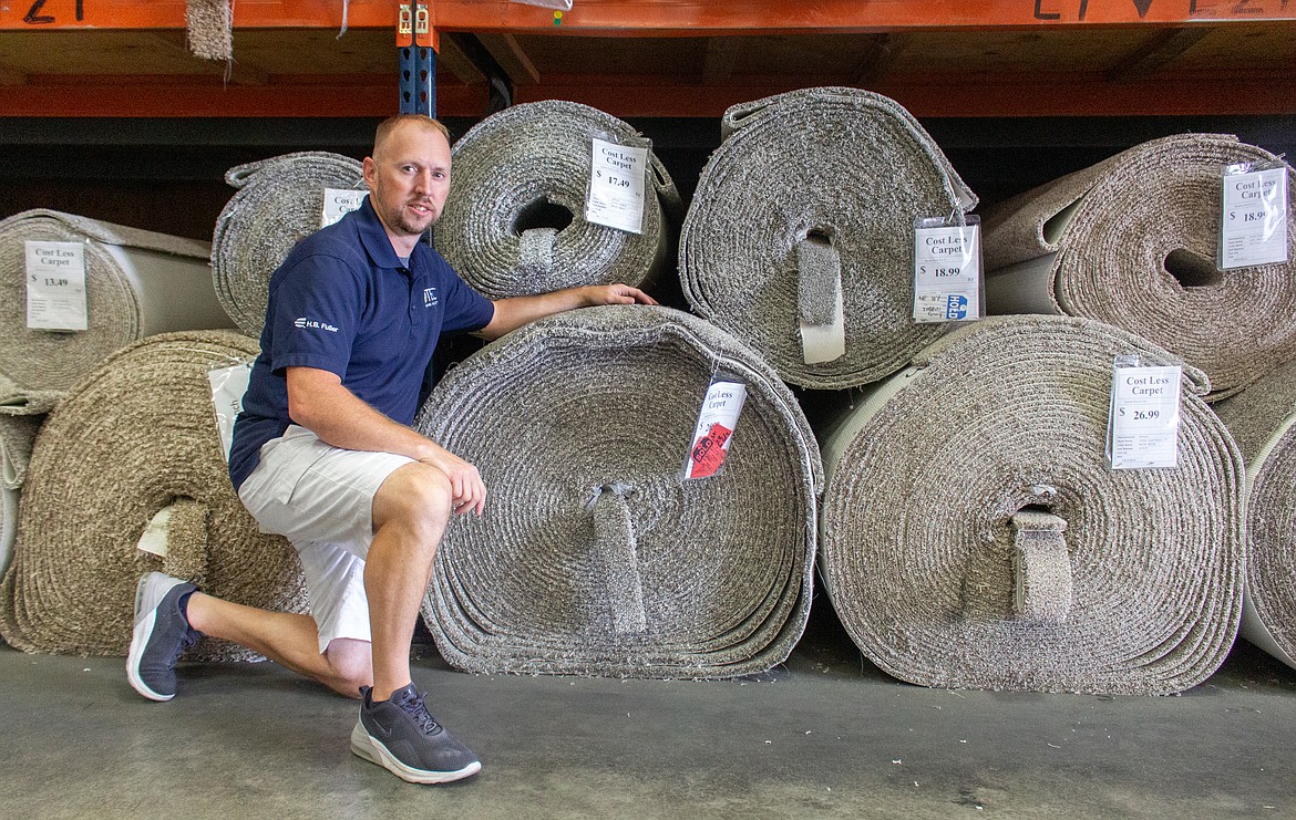 Robert “RJ” Jones, store manager for Cost Less Carpet of Moses Lake, kneels in front of rolls of carpet lining the shelves at the Moses Lake storefront.