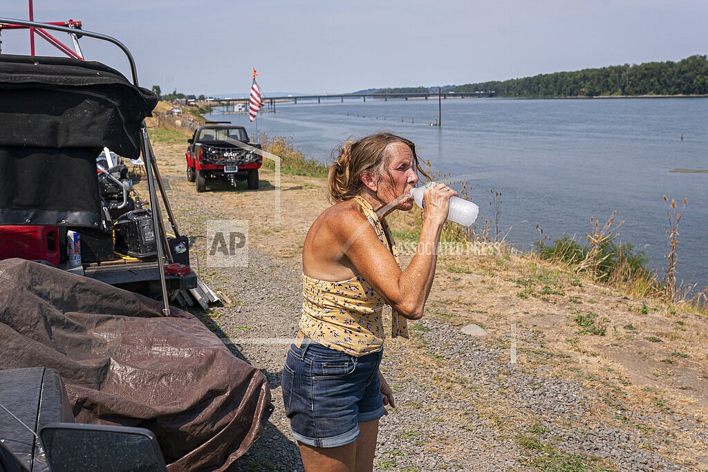 A woman living along the Columbia River who declined to be named, drinks a bottle of water delivered by Cascadia Behavioral Healthcare's street outreach team on Thursday, Aug. 12, 2021, in Portland, Ore. (AP Photo/Nathan Howard)