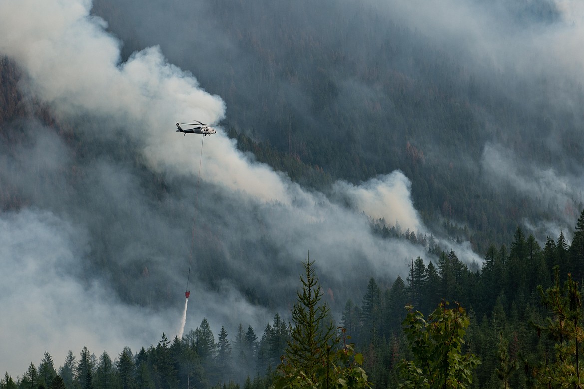 A helicopter drops a bucket of water on the Trestle Creek Fire.