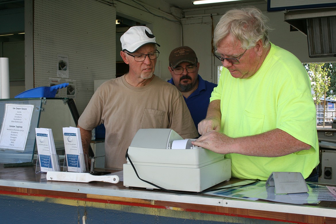 From the left, Ron Shade, William West and Dennis Foster attempt to load tape into the register at the Moses Lake Lions Club booth at the Grant County Fairgrounds Monday.