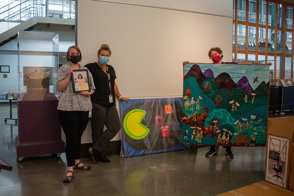 Left to right, Moses Lake Museum & Art Center staff Angela Hunt, Jenni Shelton and Dollie Boyd stand among the pieces from the “Nerd Alert!” juried art exhibition Tuesday afternoon before beginning to put pieces on the wall.