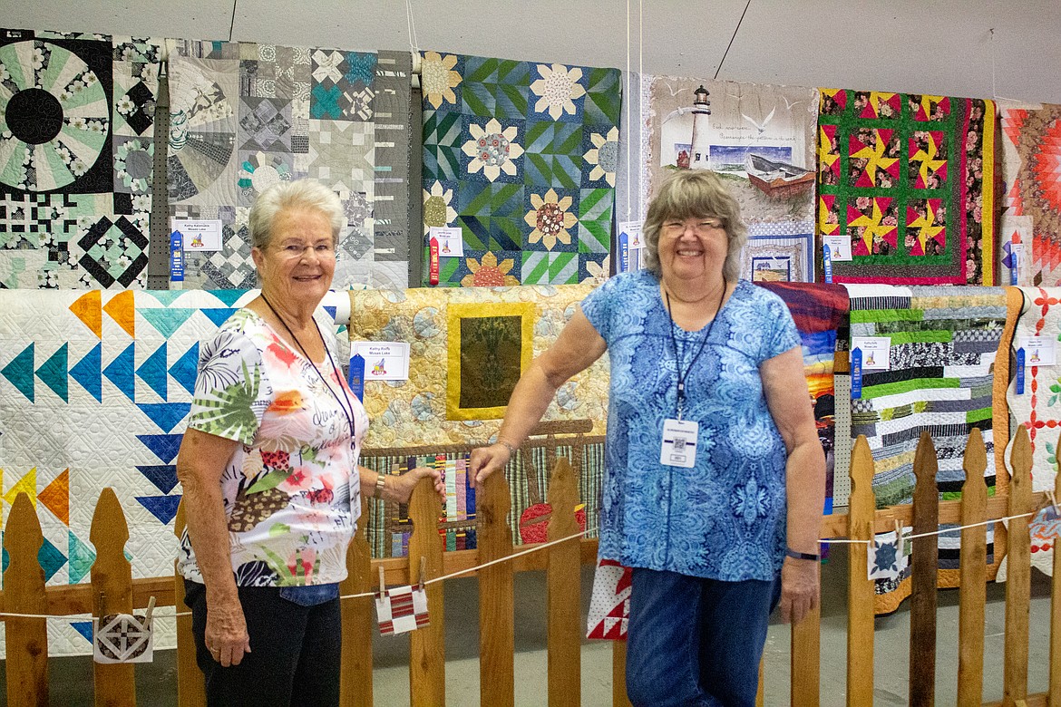 Roylene Scoggin and Barbara Bolton, superintendents of the quilt exhibit at the Grant County Fairgrounds, stand in front of quilts lining the wall in the Home Ec Building at the Grant County Fairgrounds Tuesday morning.